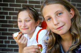 Two smiling children in school uniforms, both eating apples.