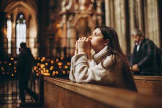 A Catholic woman kneeling in a church, praying.