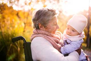 An elderly woman in a wheelchair cholding a baby and smiling