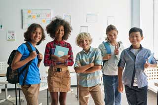 Five smiling school children, standing in a classroom