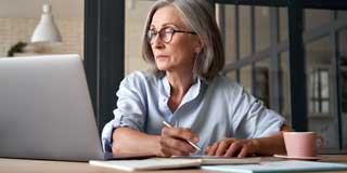 A professional attending a webinar on her laptop while taking notes