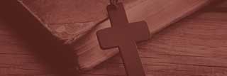 A colorized image of a crucifix leaning against a bible on a wooden table.